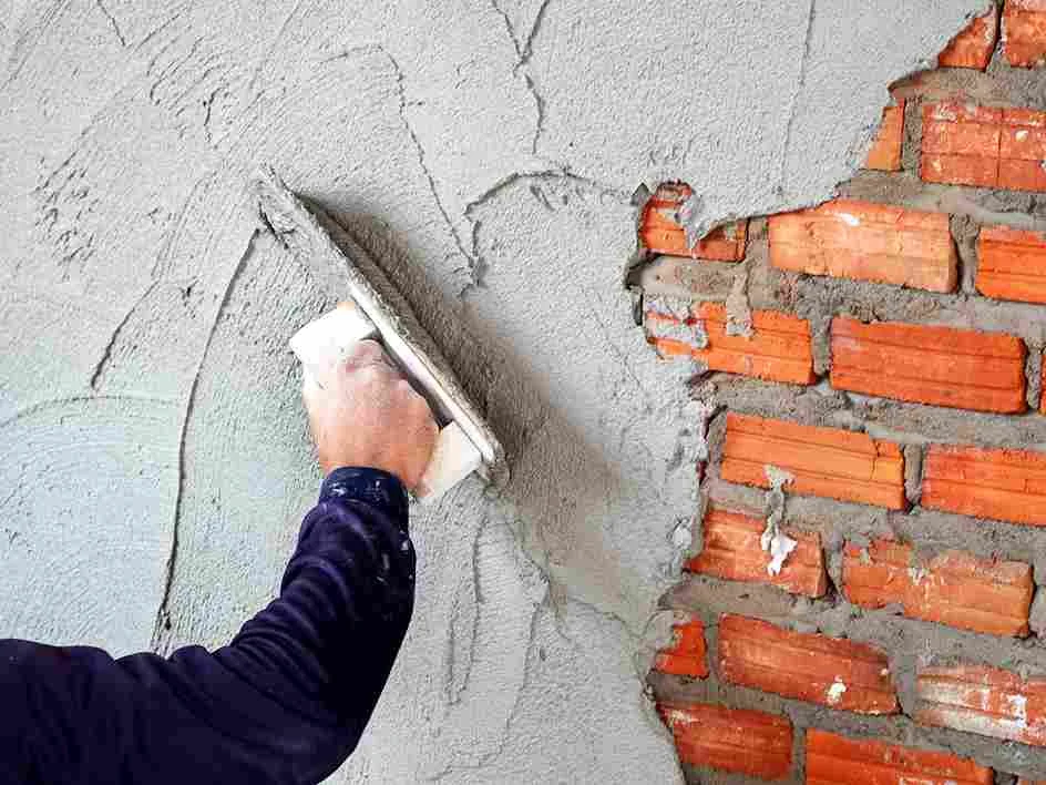 Applying cement render over exposed brick wall during renovation in Surrey.