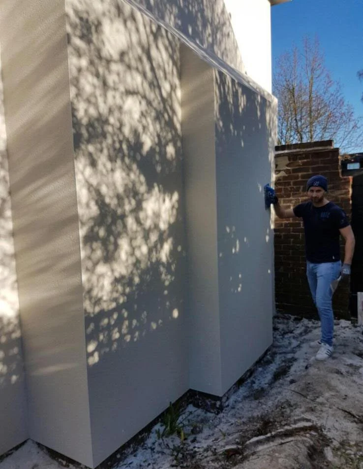 Worker painting freshly rendered exterior wall during renovation project in Surrey.