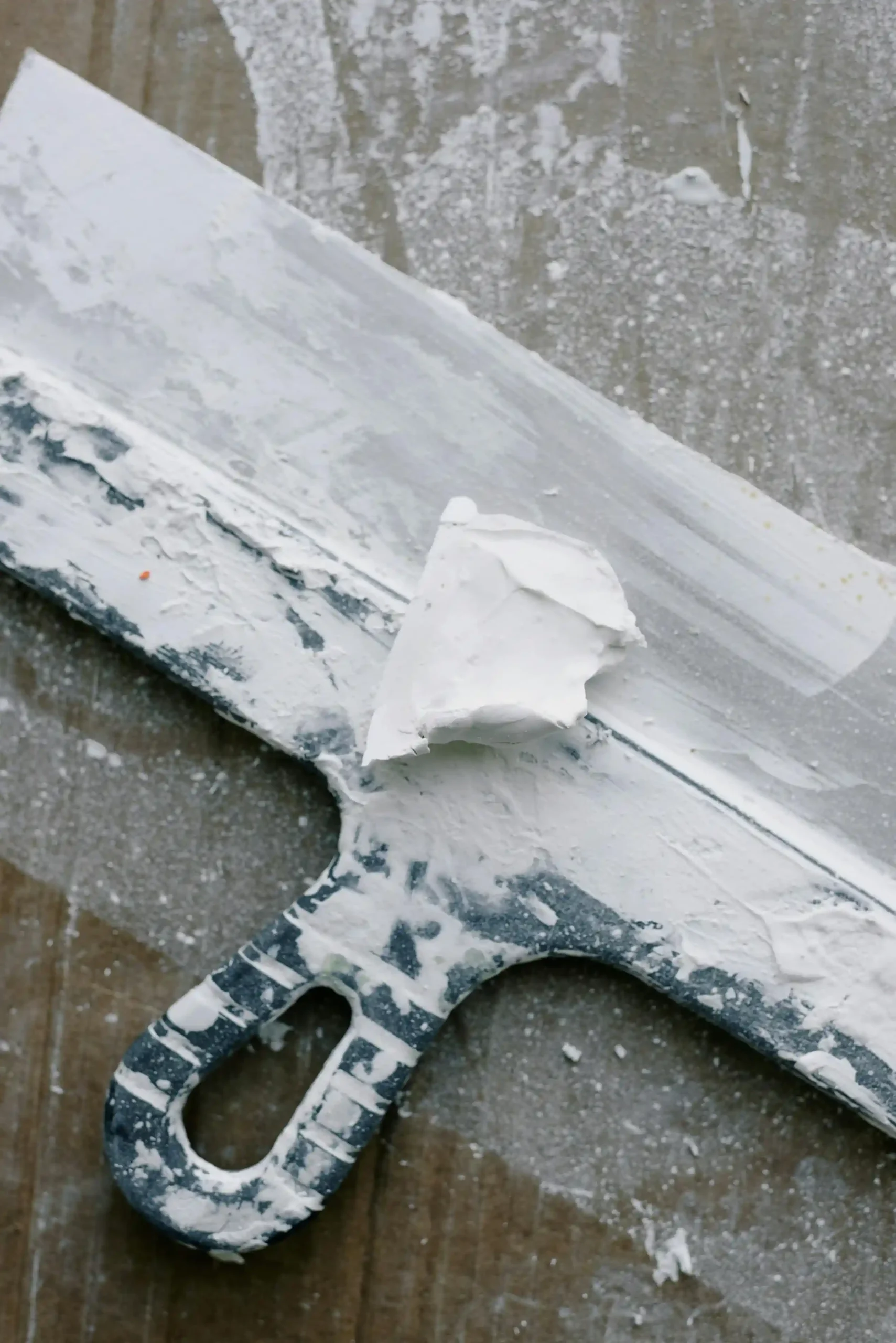 Metal plastering scraper covered in fresh plaster during wall finishing work.