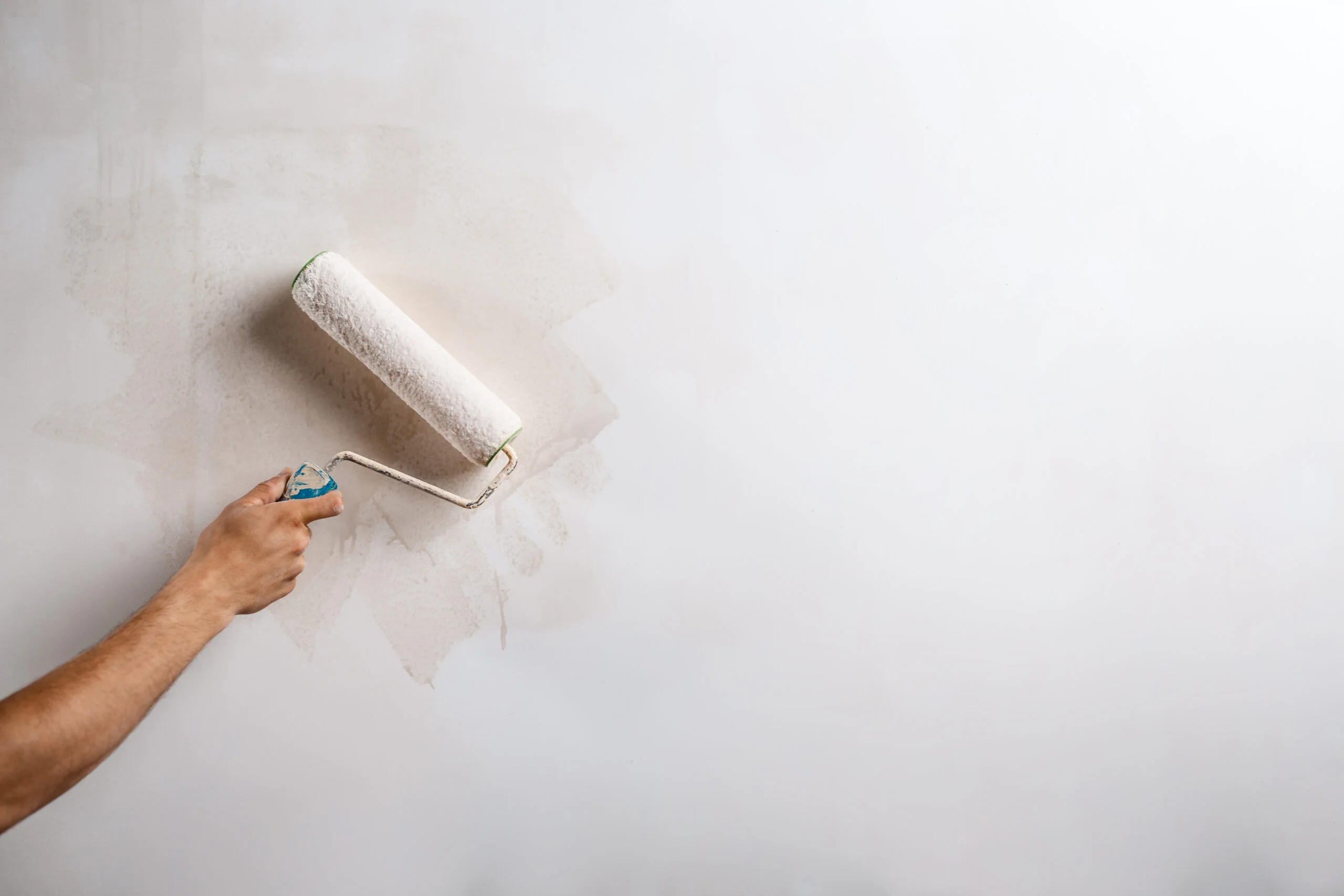 Paint roller applying fresh paint to smooth plastered wall in Surrey.