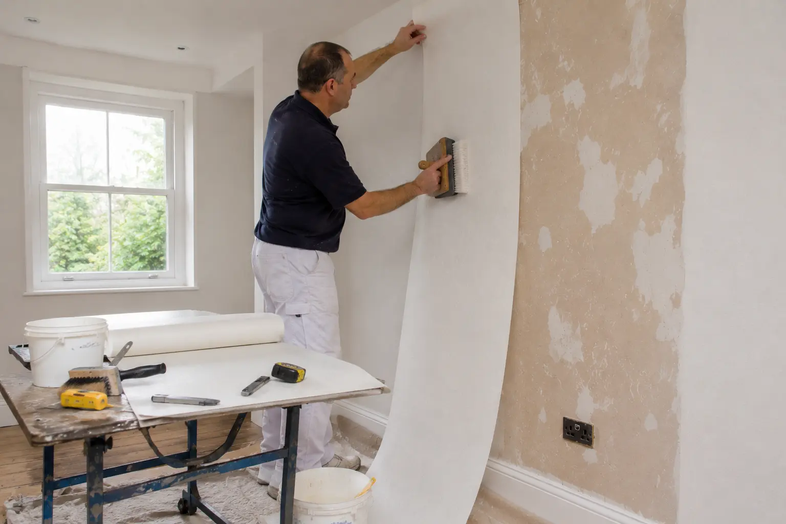 Decorator hanging a strip of lining paper using a smoothing brush technique