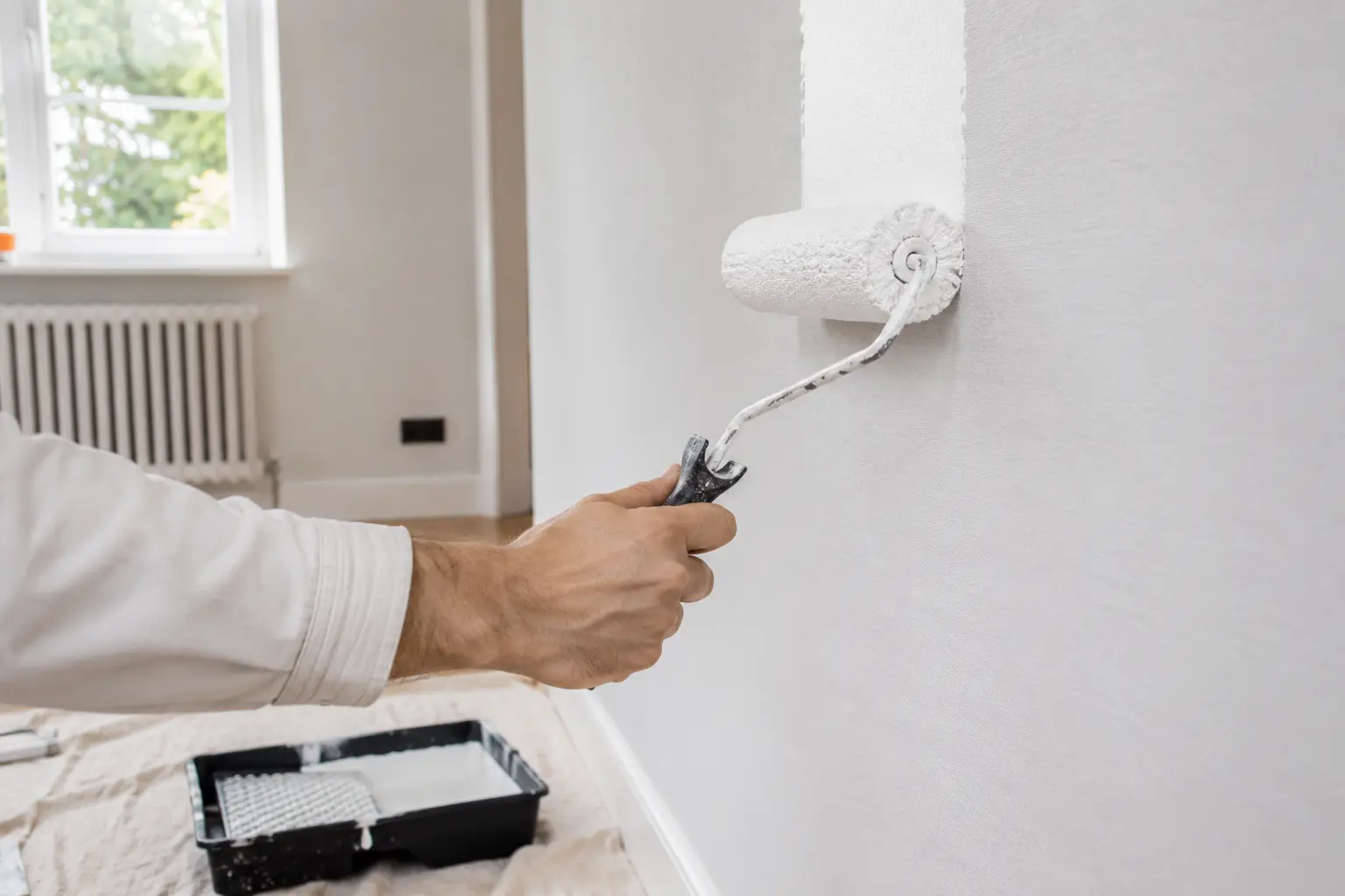 Painter applying emulsion paint over a wall lined with lining paper