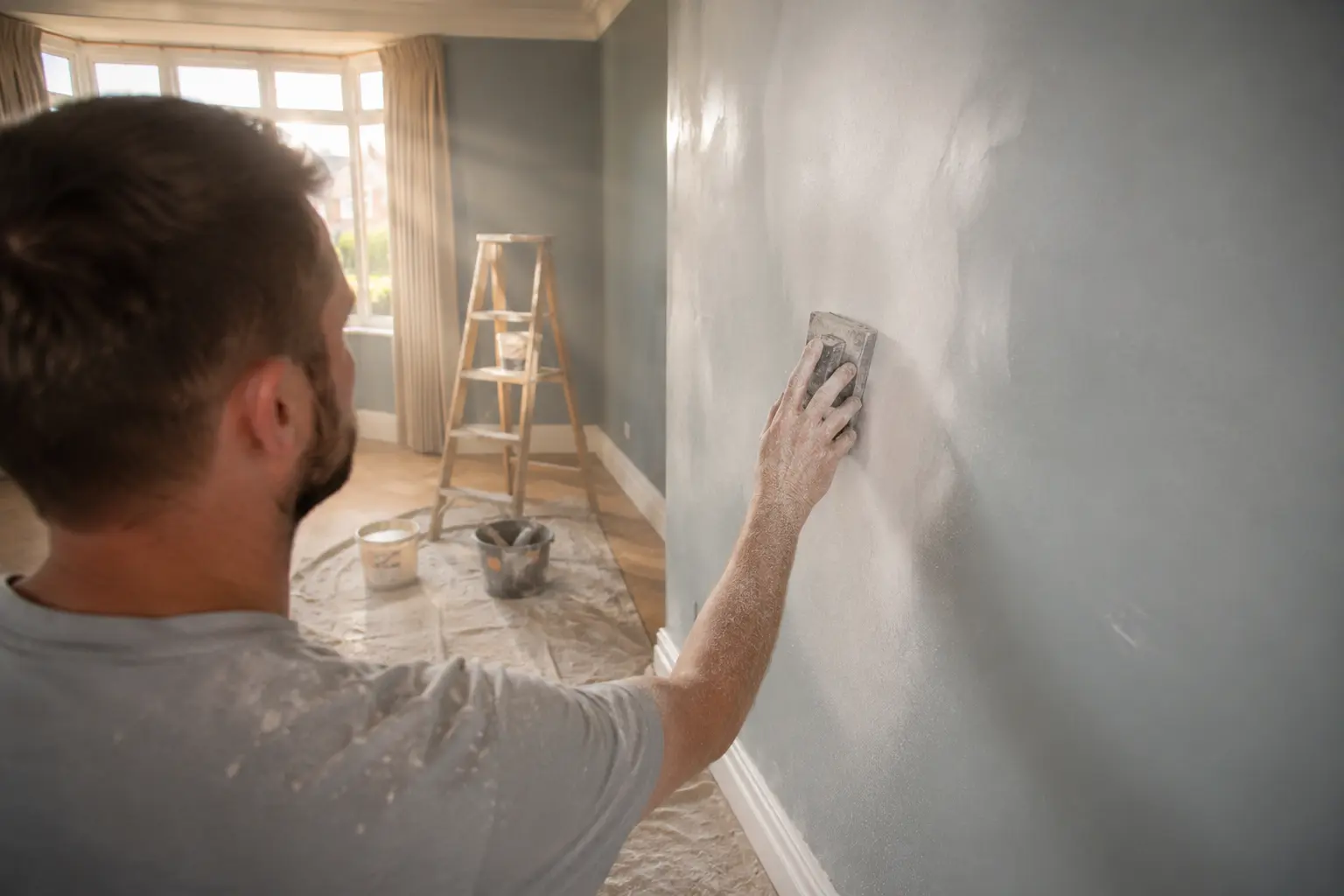 Sanding a rough interior wall surface as an alternative to skim coating.